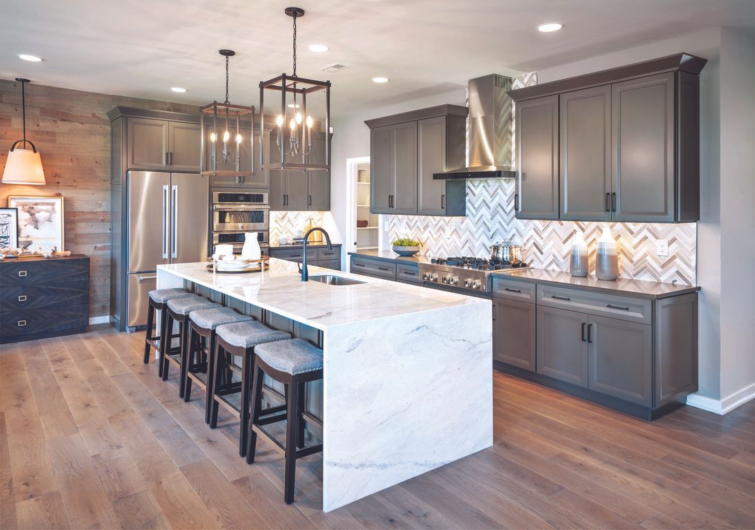 Modern kitchen with gray cabinets, white island, and stainless steel appliances.