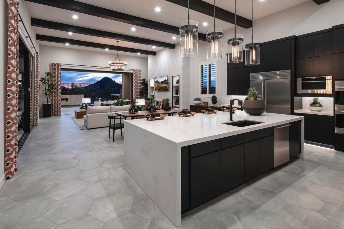 Modern kitchen with island, dark cabinets, and a view of the living room and outdoor scenery.