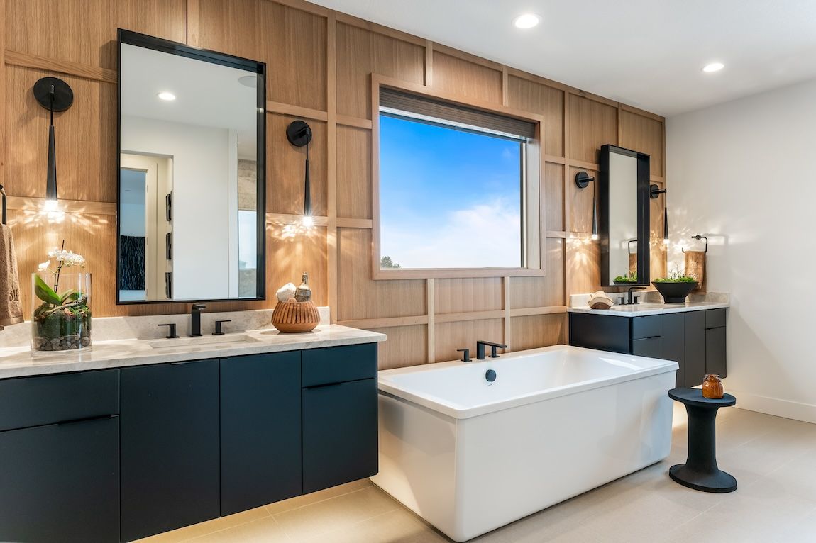 Modern bathroom with wood panel walls, dark blue vanities, a white tub, and a window with a blue sky.
