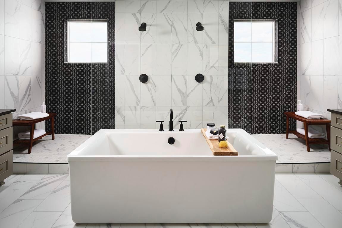 Modern bathroom with a white tub, marble walls, black fixtures, and patterned tile.