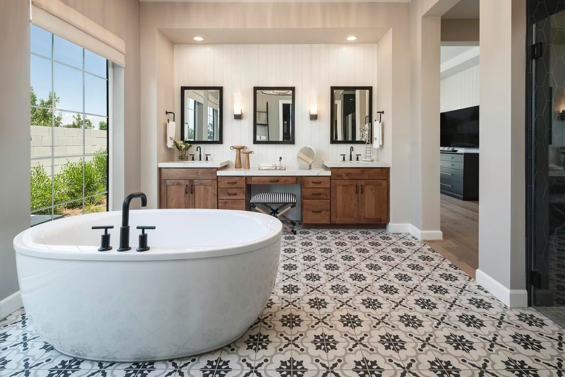 Spacious bathroom with a freestanding tub and a vanity with three mirrors and brown cabinets.