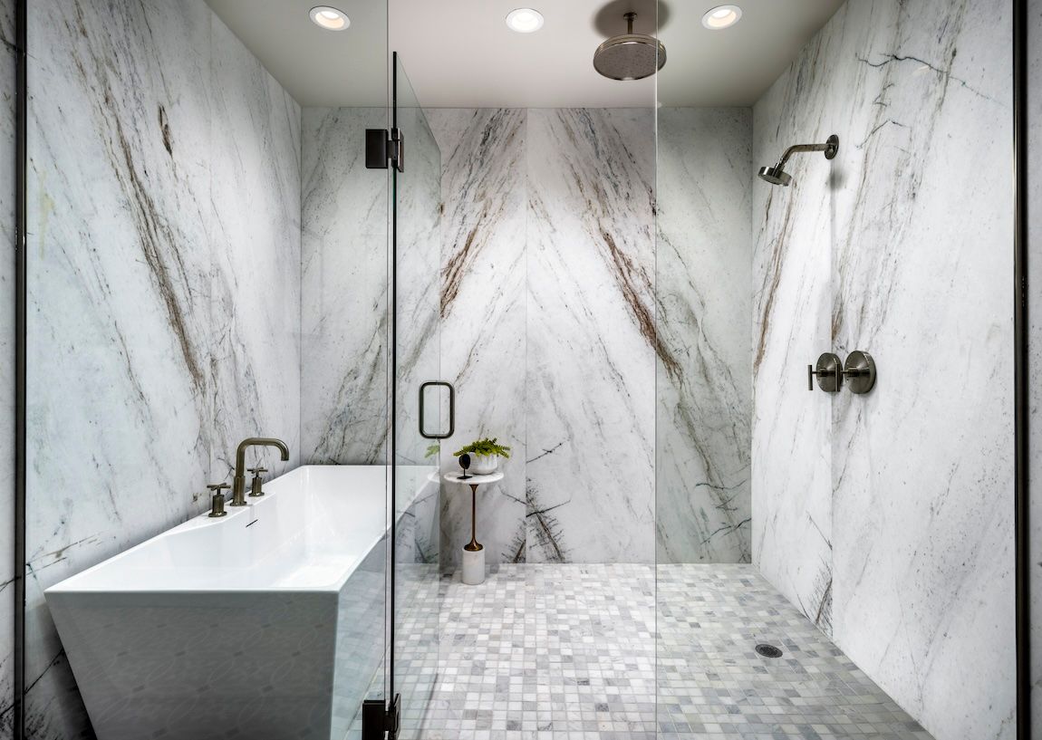 Modern bathroom with white marble walls, glass shower, and white square tub.