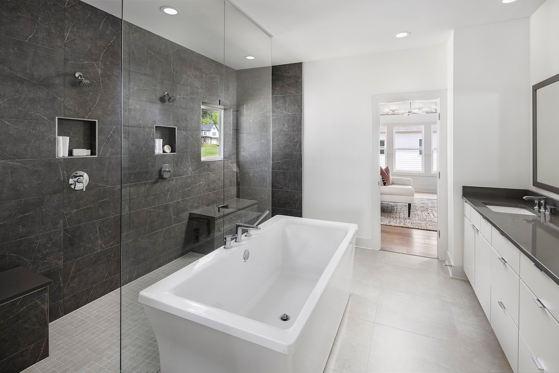Modern bathroom: dark gray tiled shower, white tub, white cabinets, and bright lighting.