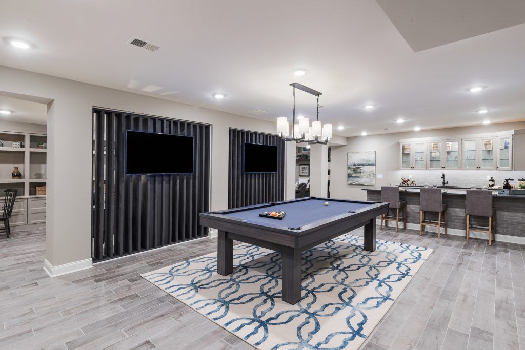 A finished basement with a pool table, bar, and two TVs on black textured walls.