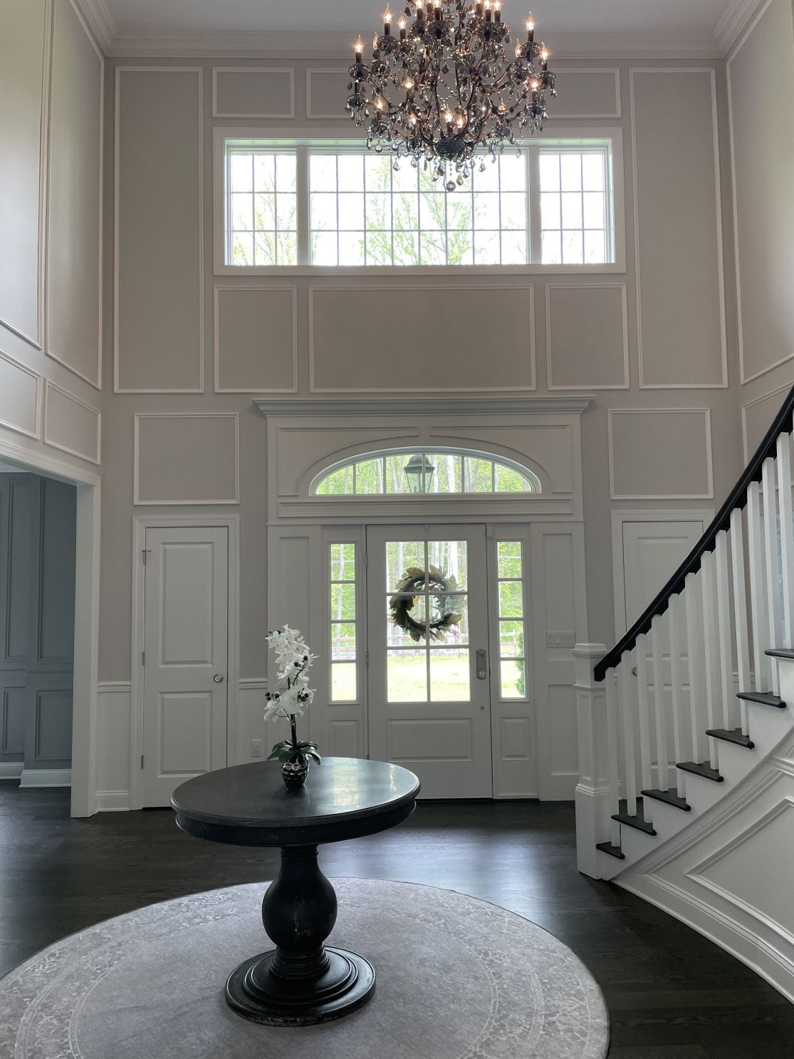 A grand entryway with a staircase, chandelier, and a round table with a floral arrangement.