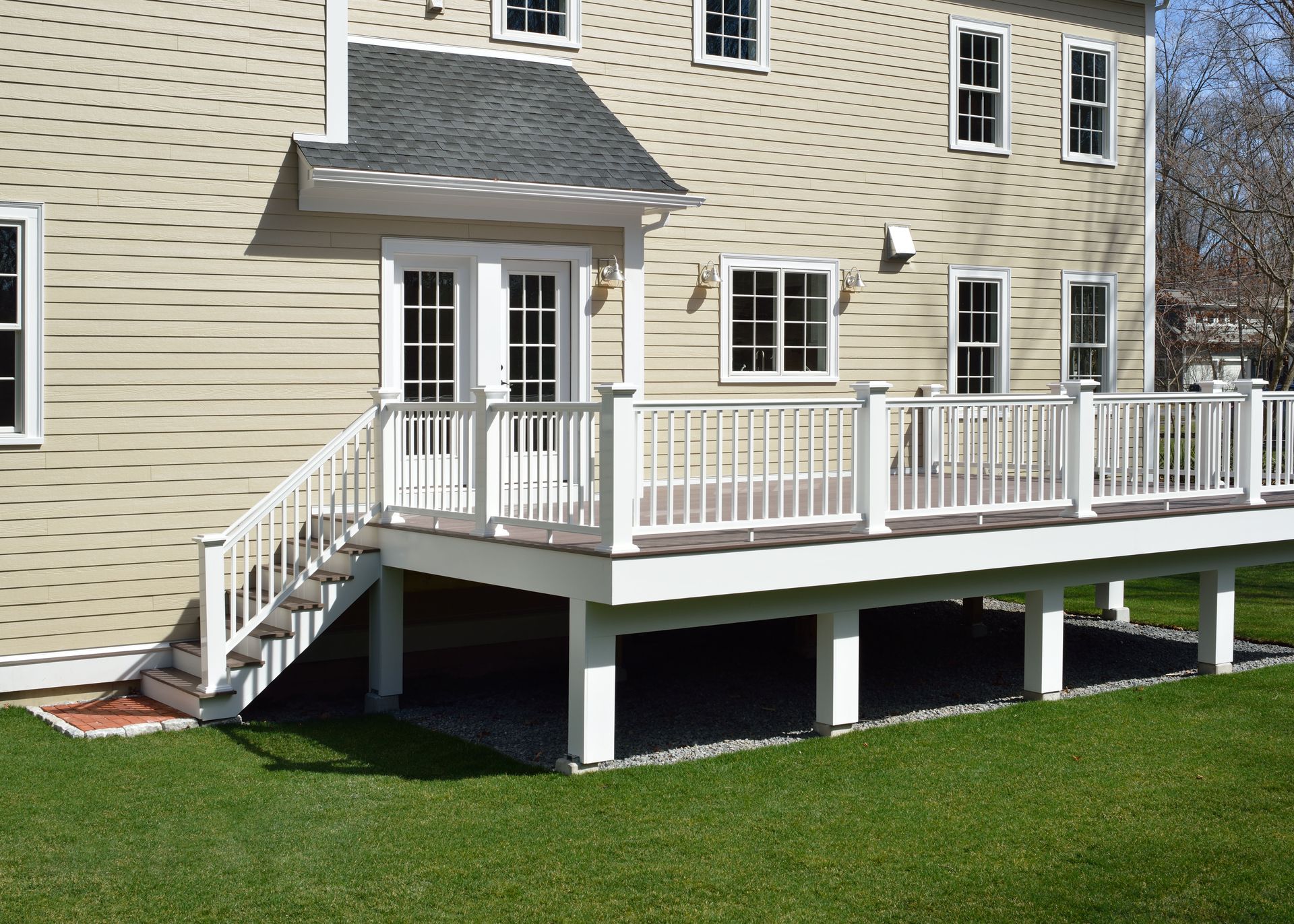 White deck attached to a light-colored house. Stairs lead down to a grassy lawn.