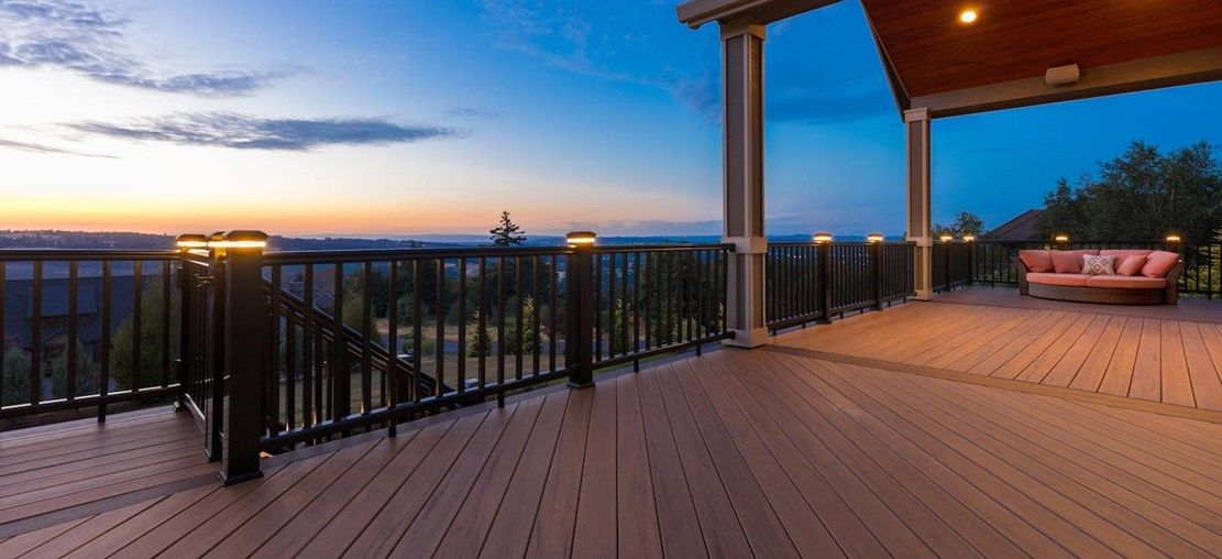 A wooden deck overlooking a scenic landscape at dusk, with a seating area and railing lights.