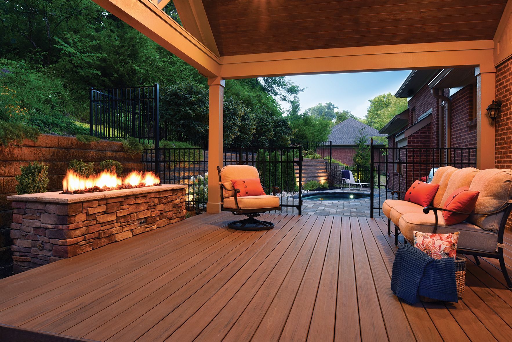 Covered wooden patio with fire pit, seating, and view of a yard and trees.