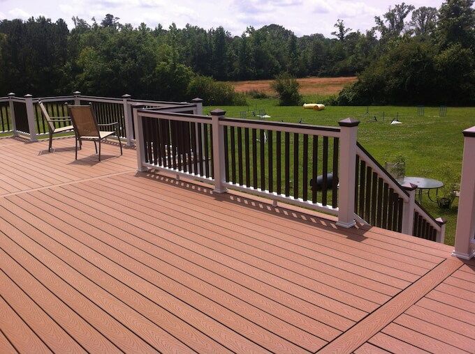 Composite deck with white railings, brown accents, and a chair overlooking a grassy field.