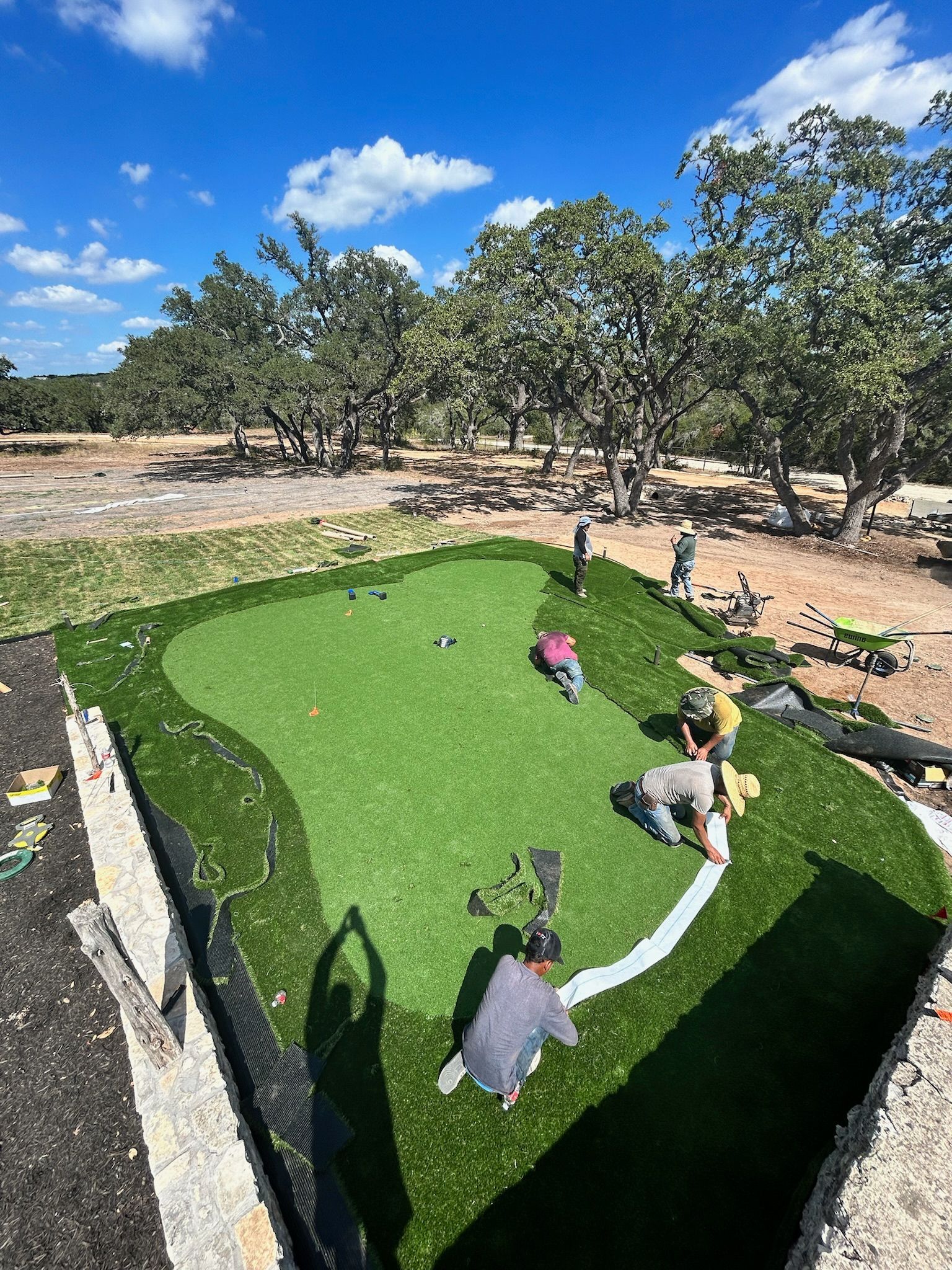 People playing mini golf on a bright green course under a blue sky with trees around them.