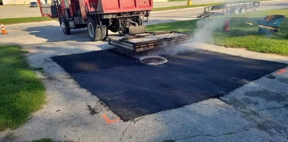 Asphalt paving a square section of a road, a red truck in the background.