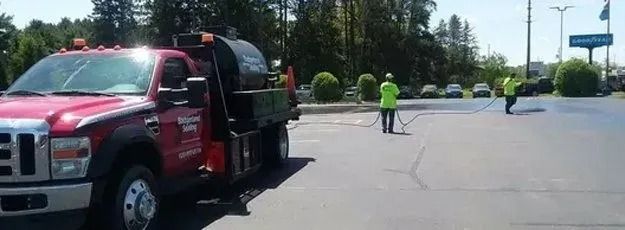 Red truck with workers in neon vests, spraying a parking lot.