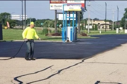 Worker in safety vest seals asphalt cracks at gas station.