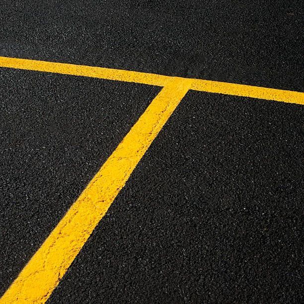 Yellow painted lines on black asphalt, forming a T-shape, likely marking a road.