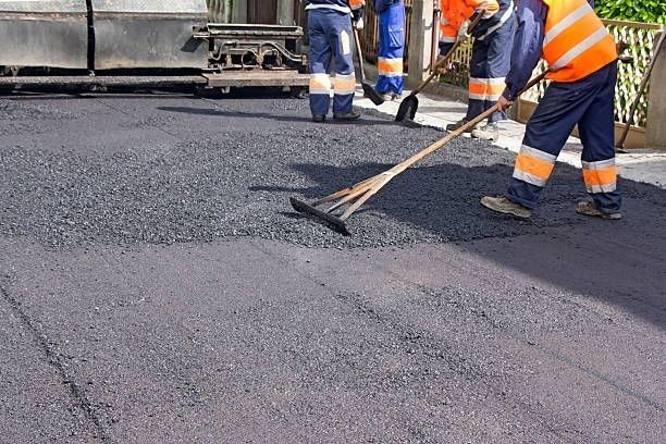 Road workers spreading asphalt with rakes, near a paving machine.