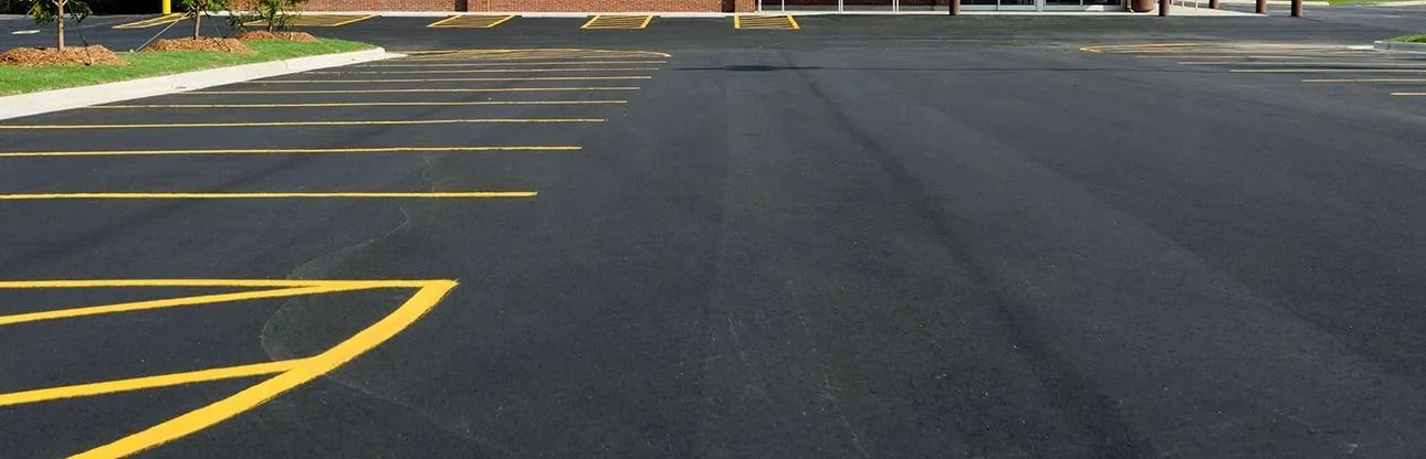 An empty parking lot with yellow painted parking space lines. Asphalt surface with a building in the background.