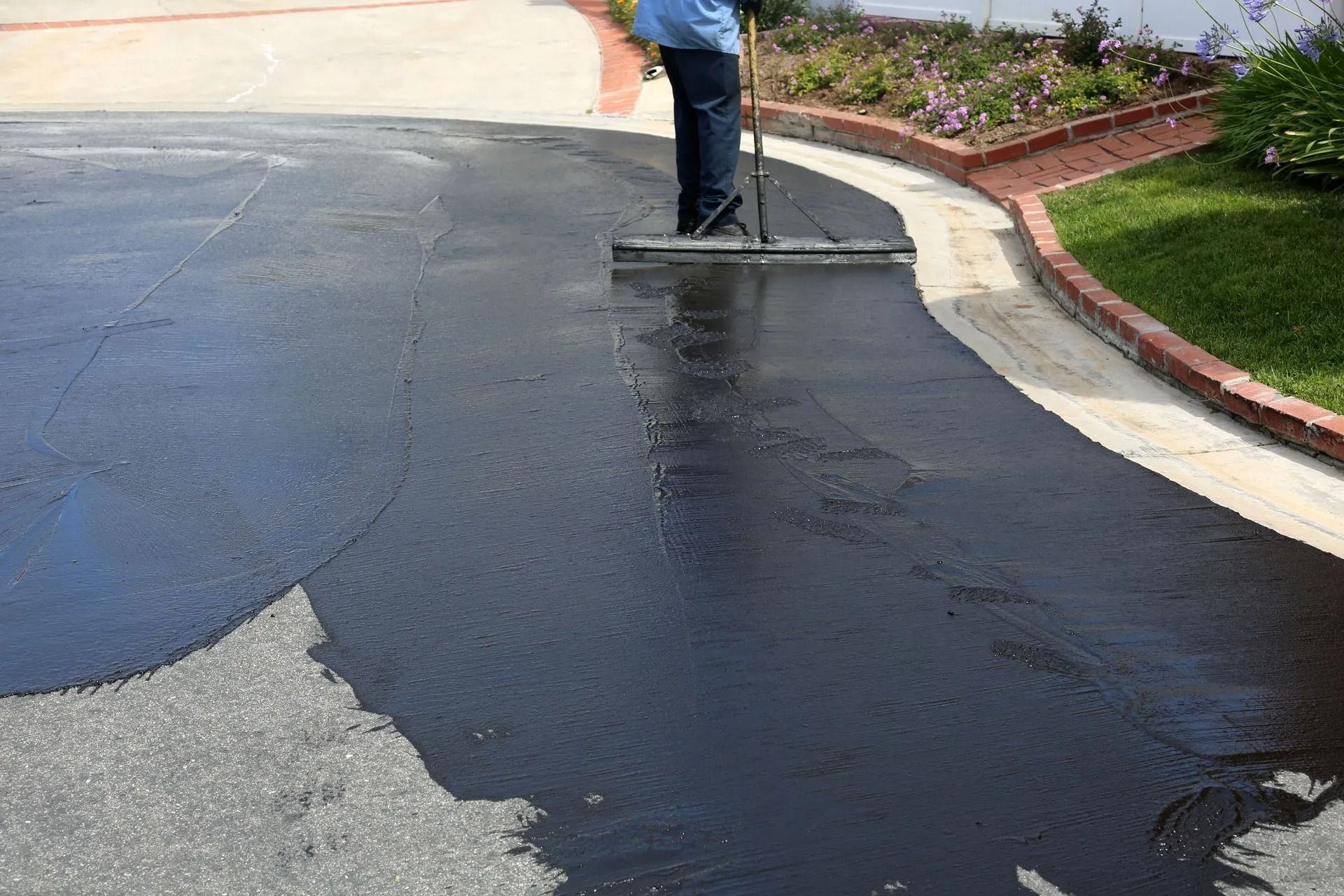Person applying black sealant to asphalt driveway with squeegee.