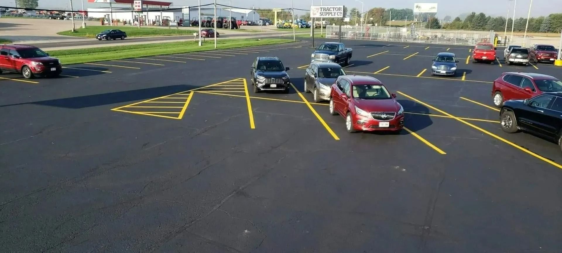 Cars in a parking lot with yellow painted lines and cones, with buildings in the background.