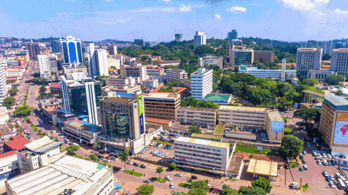 Aerial view of a bustling cityscape in Kampala, Uganda, with tall buildings, green spaces, and busy streets under a clear sky.