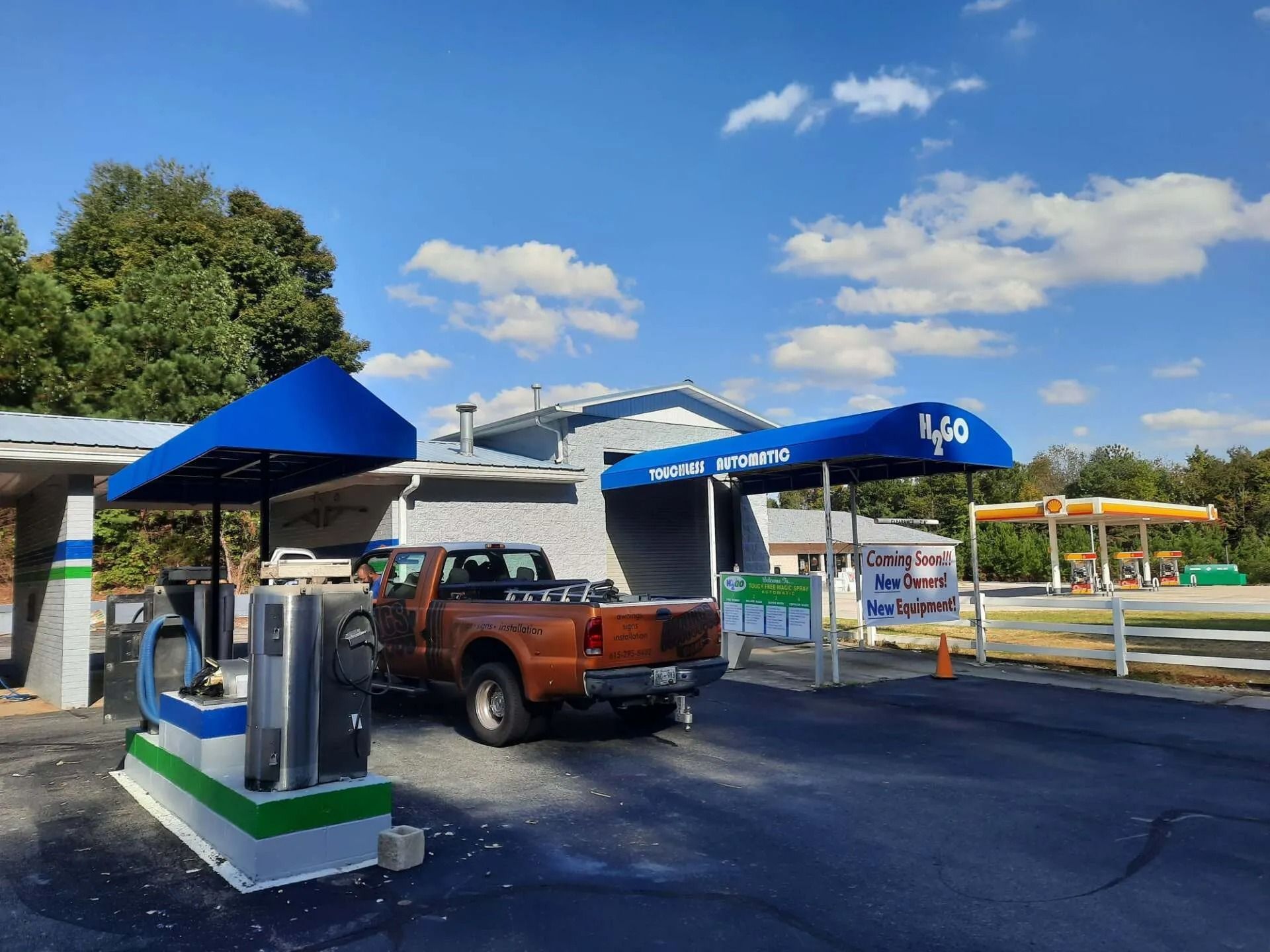 A copper pickup truck parked at a gas station with blue awnings under a bright blue sky.