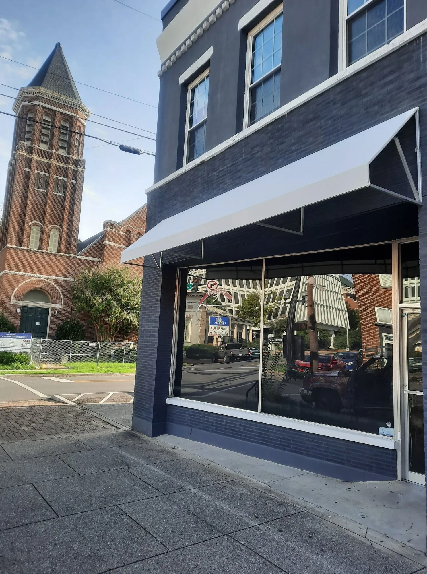 A blue-painted storefront with a white awning stands next to a tall, historic brick church with a steeple.