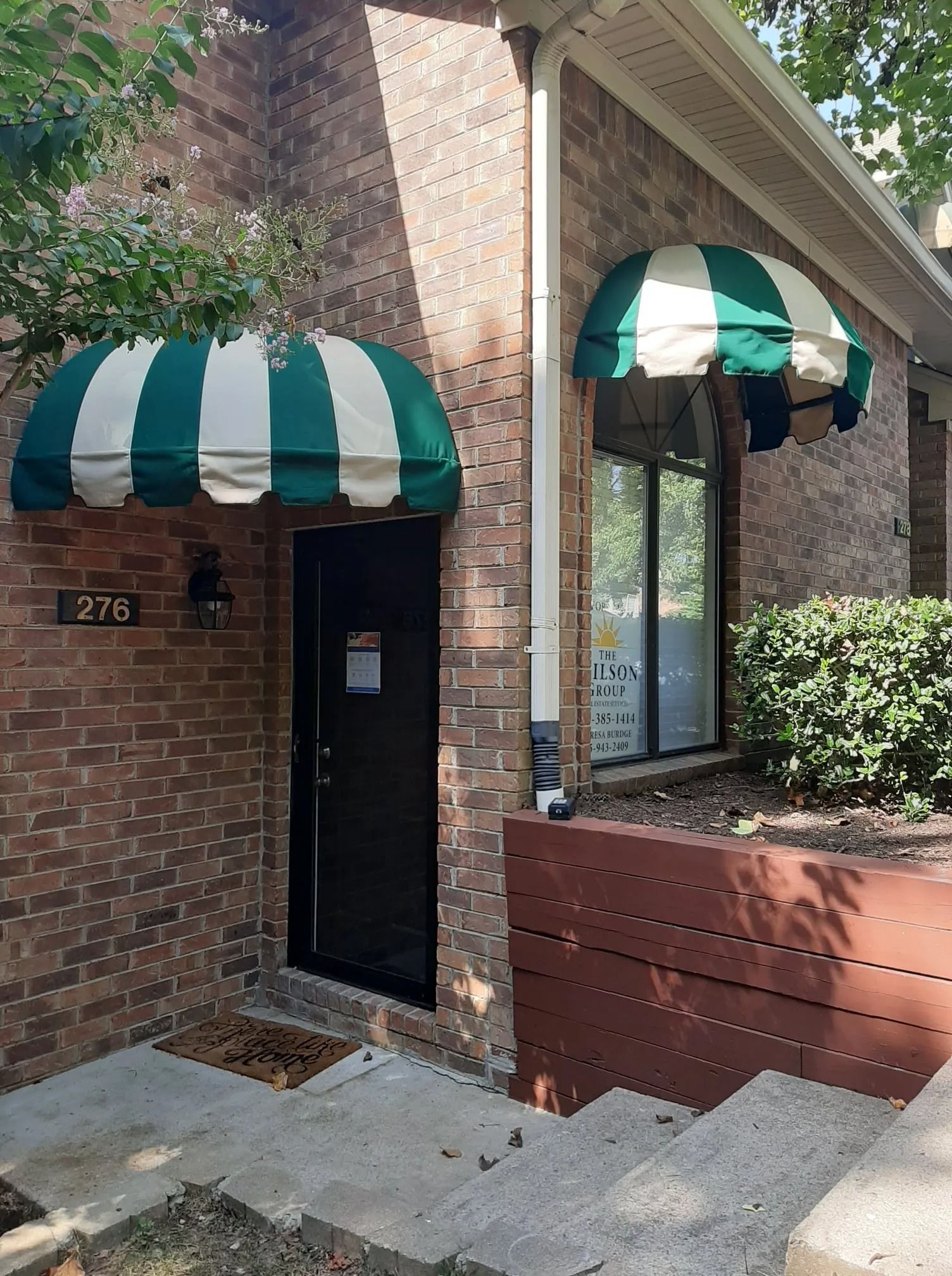 A brick building entrance labeled 275 with green and white striped awnings over the black door and adjacent window.