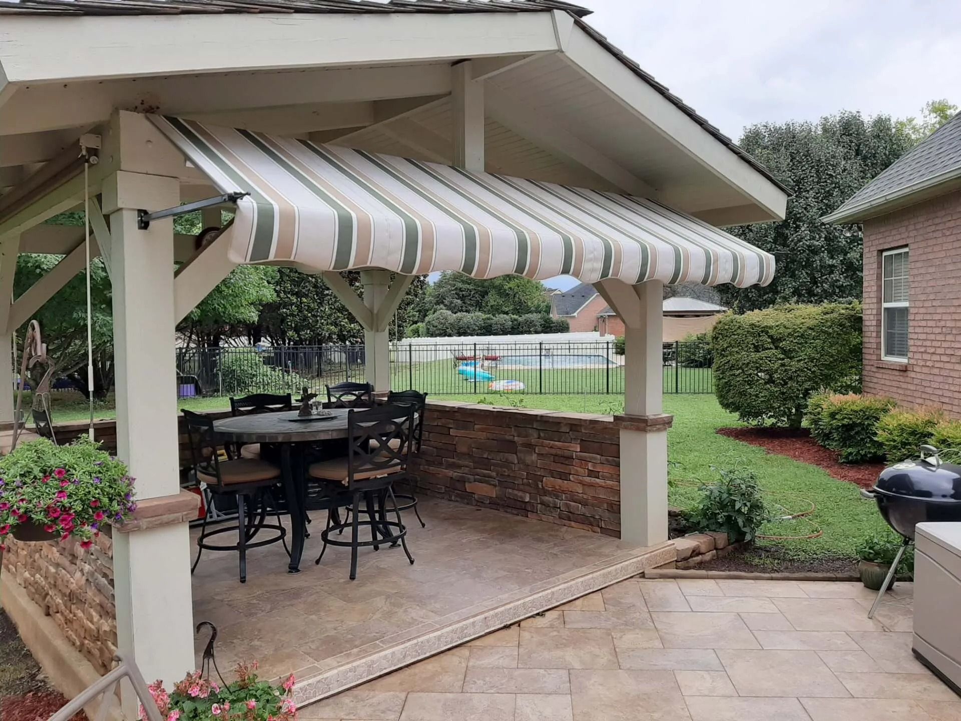 A patio with stone walls and columns, featuring a striped retractable awning over a dining table and chairs.