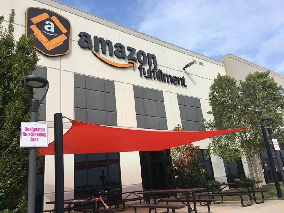 Exterior view of an Amazon fulfillment center building with an orange shade sail covering an outdoor seating area.