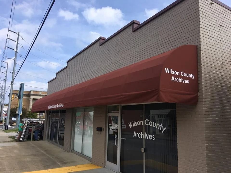 The Wilson County Archives building, a brick storefront with a red awning under a bright blue sky.