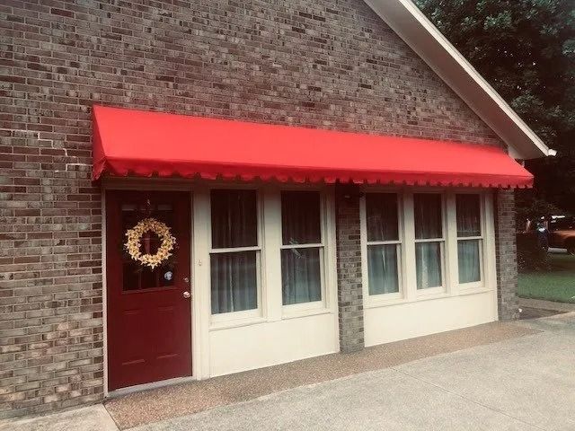 A brick building exterior with a bright red awning over a matching red door and multiple windows with white frames.