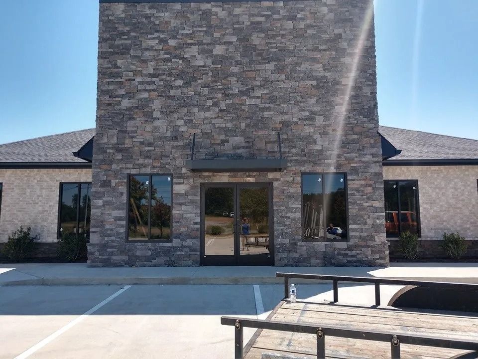 Commercial building entrance with a stone facade, glass doors, and parking area on a sunny day.
