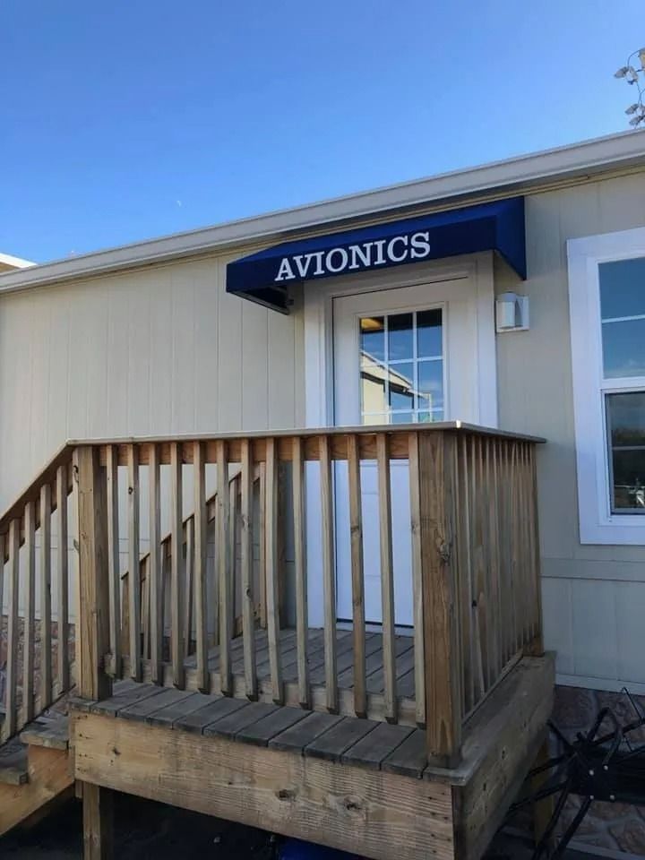 A wooden staircase leading to a white door with a dark blue awning labeled 