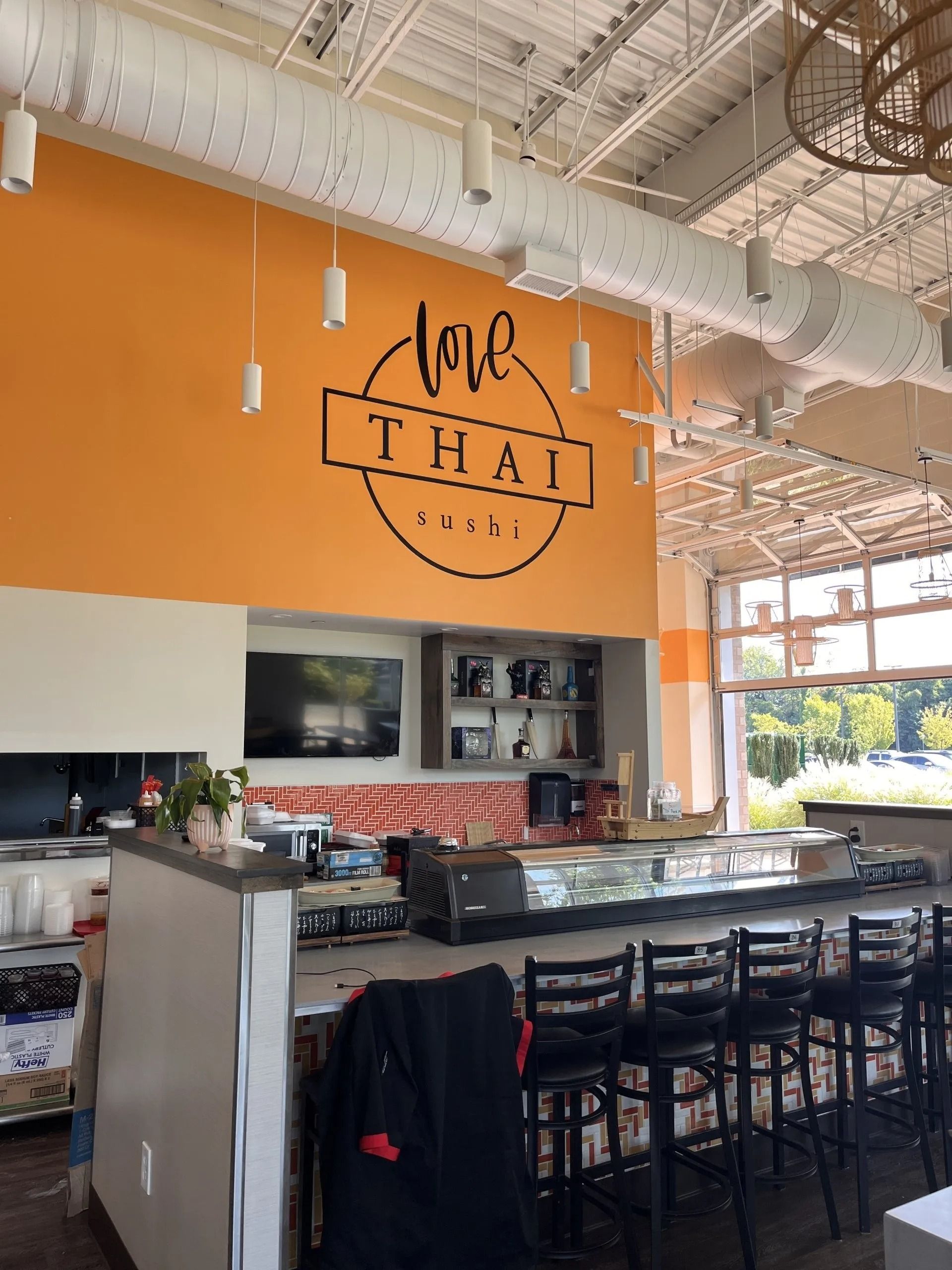 Interior view of Love Thai restaurant featuring a bright orange wall with the logo, a bar counter, and stools.