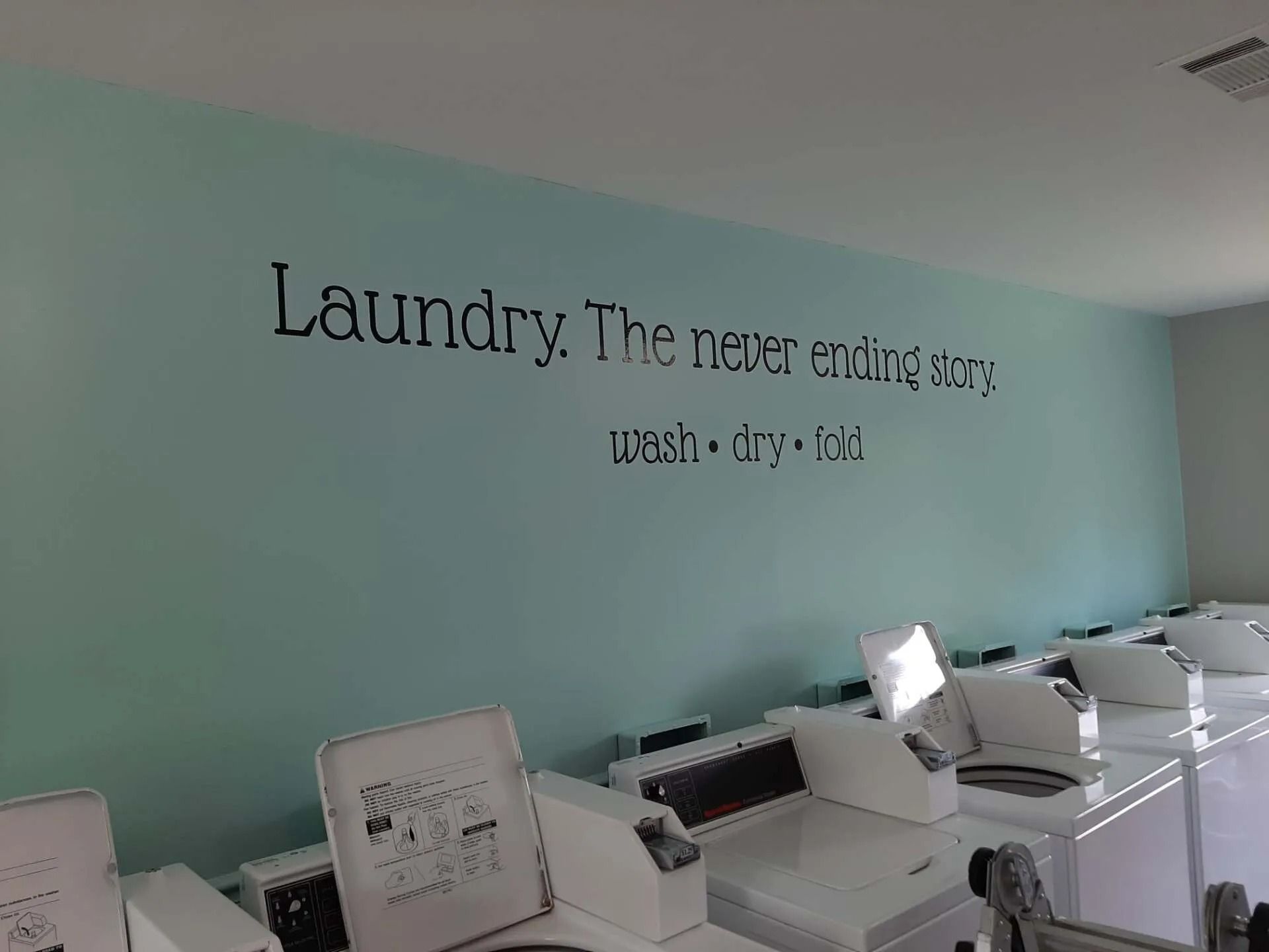 Rows of white washing machines against a light blue wall with black wall decal text: 