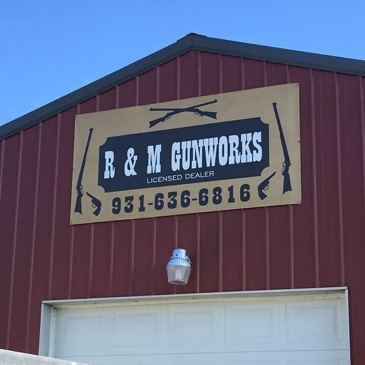 A sign for R & M Gunworks with a phone number mounted on the exterior of a red metal building.