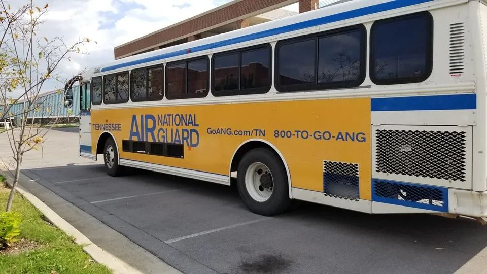 Yellow and white Air National Guard bus parked in an outdoor lot on a sunny day.