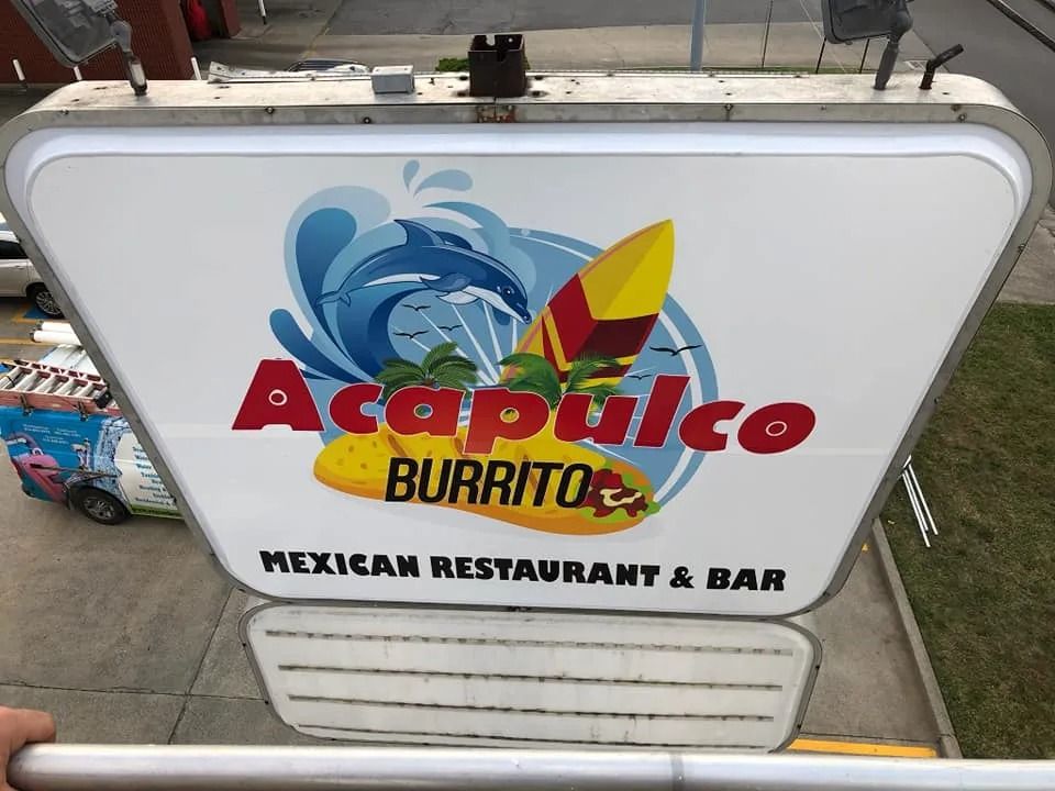 Sign for Acapulco Burrito Mexican Restaurant & Bar, featuring a surfboard and wave graphic, viewed from above.