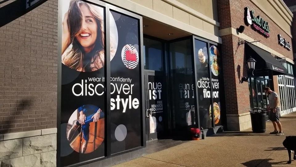 Storefront with window decals featuring photos of a smiling person and food, with text saying 