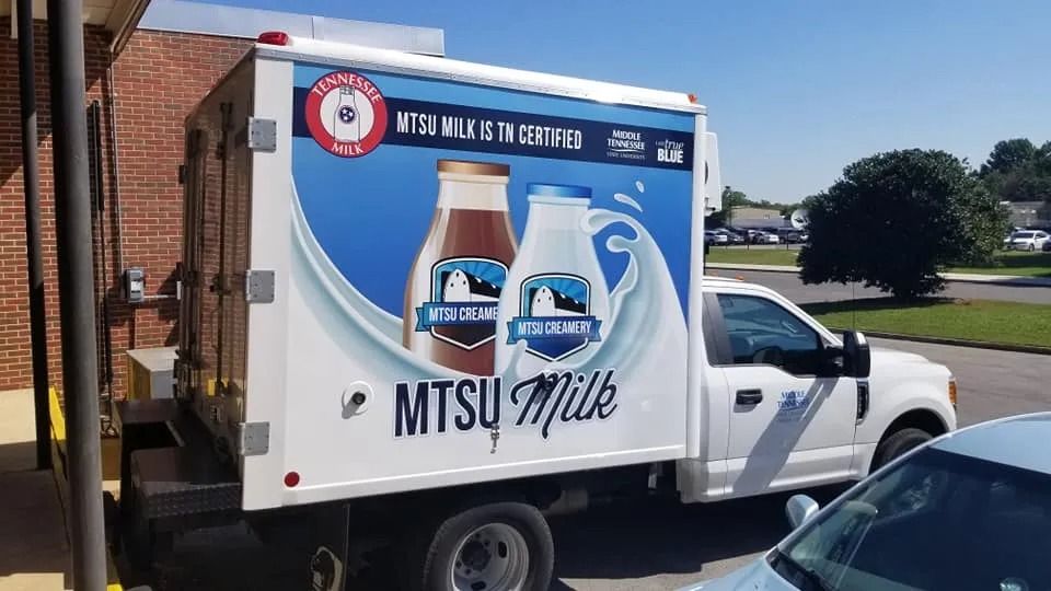 A white delivery truck parked outside, featuring advertisements for MTSU Milk with images of chocolate and white milk.