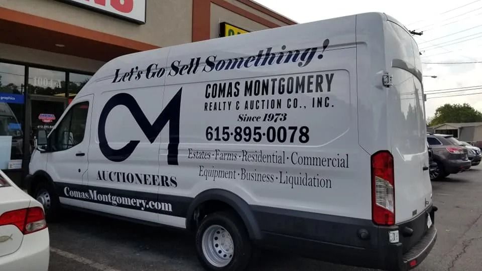 A white Comas Montgomery Realty & Auction Co. van parked in front of a building.