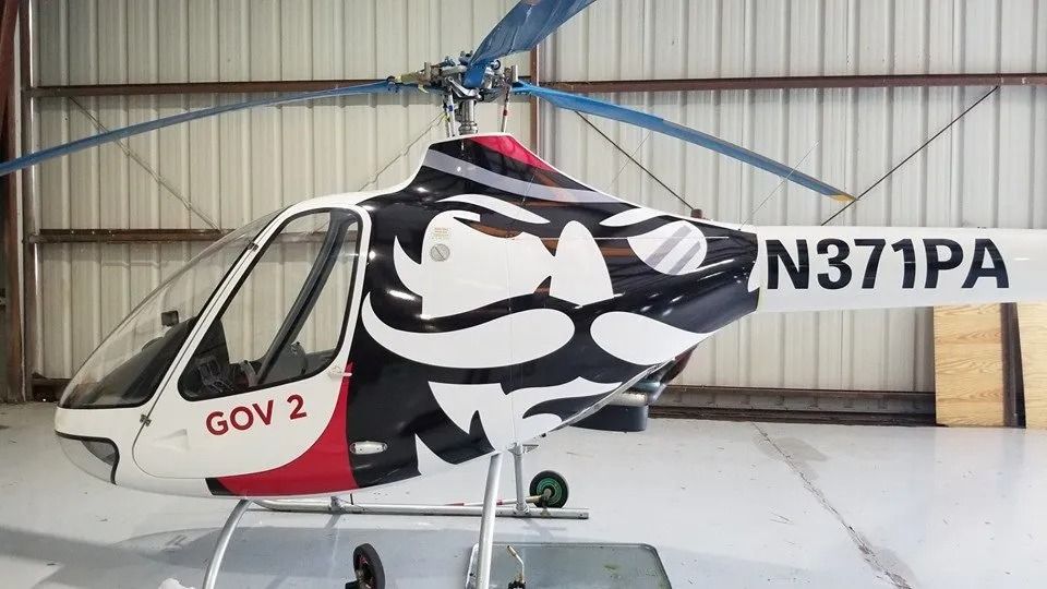 A white and red helicopter with a prominent black and white mustache decal in a hangar with the registration N371PA.