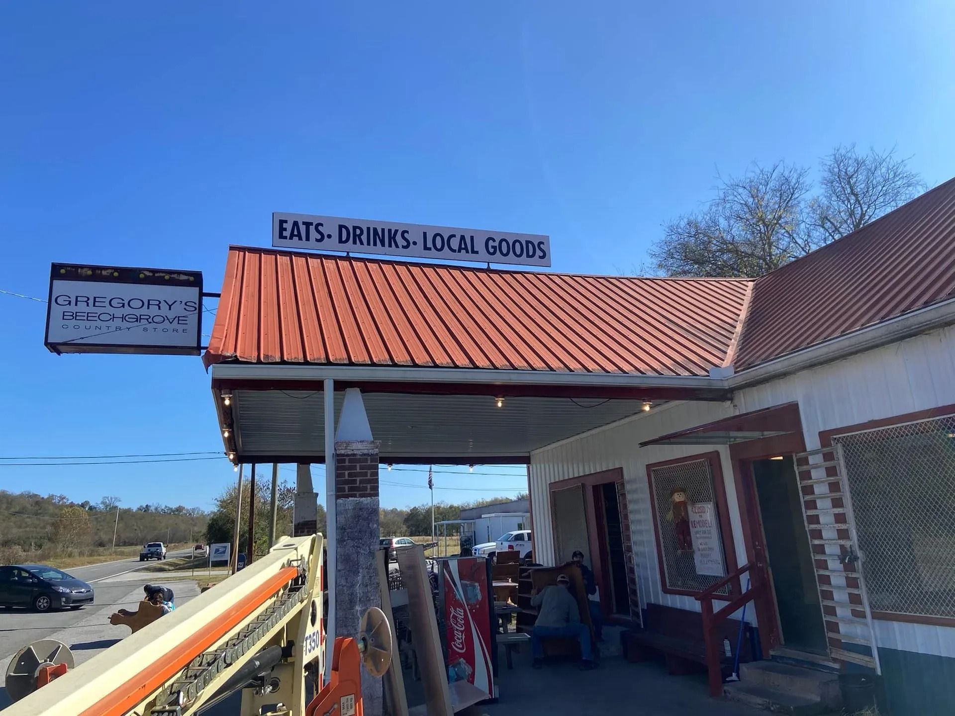 A white country store with a red metal roof under a blue sky, featuring a sign that reads 