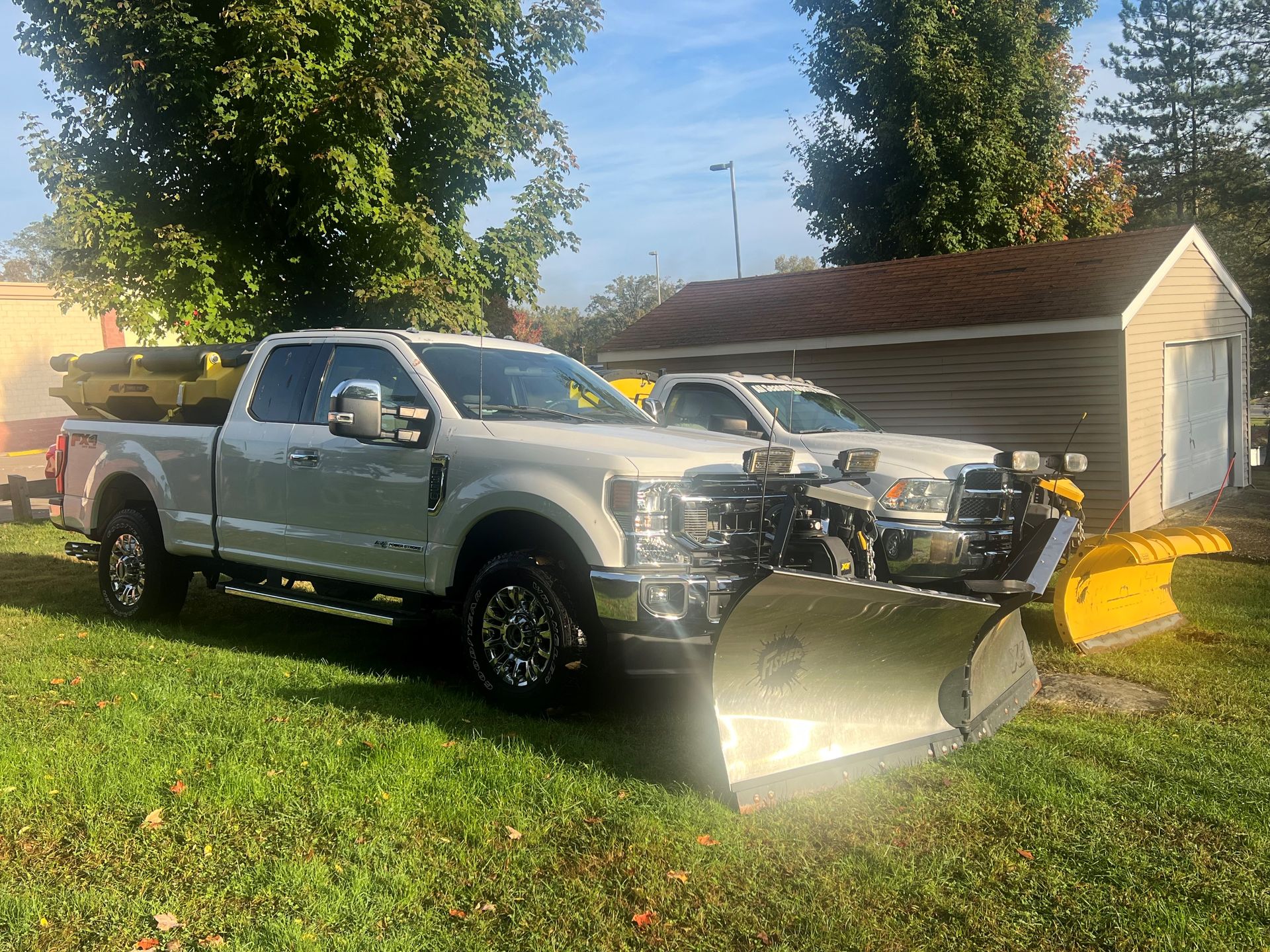 A white truck with a snow plow attached to it is parked in the grass.