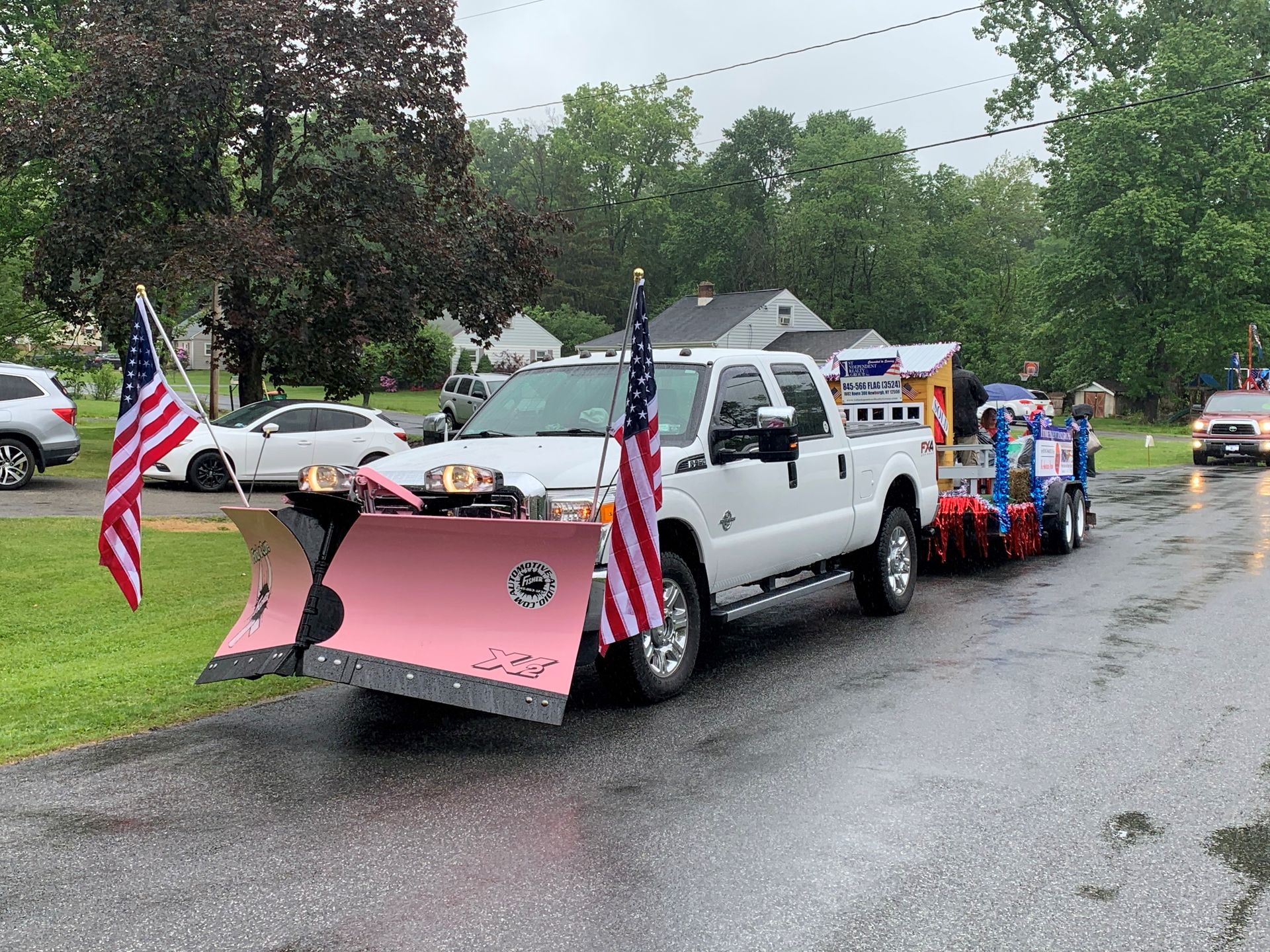 A white truck with a pink snow plow attached to it is parked on the side of the road.