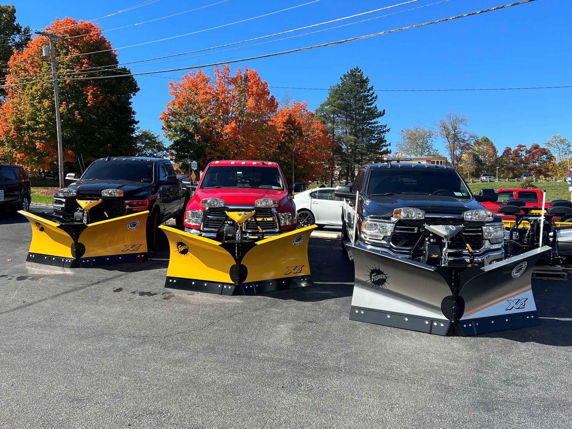 A row of snow plows are parked in a parking lot
