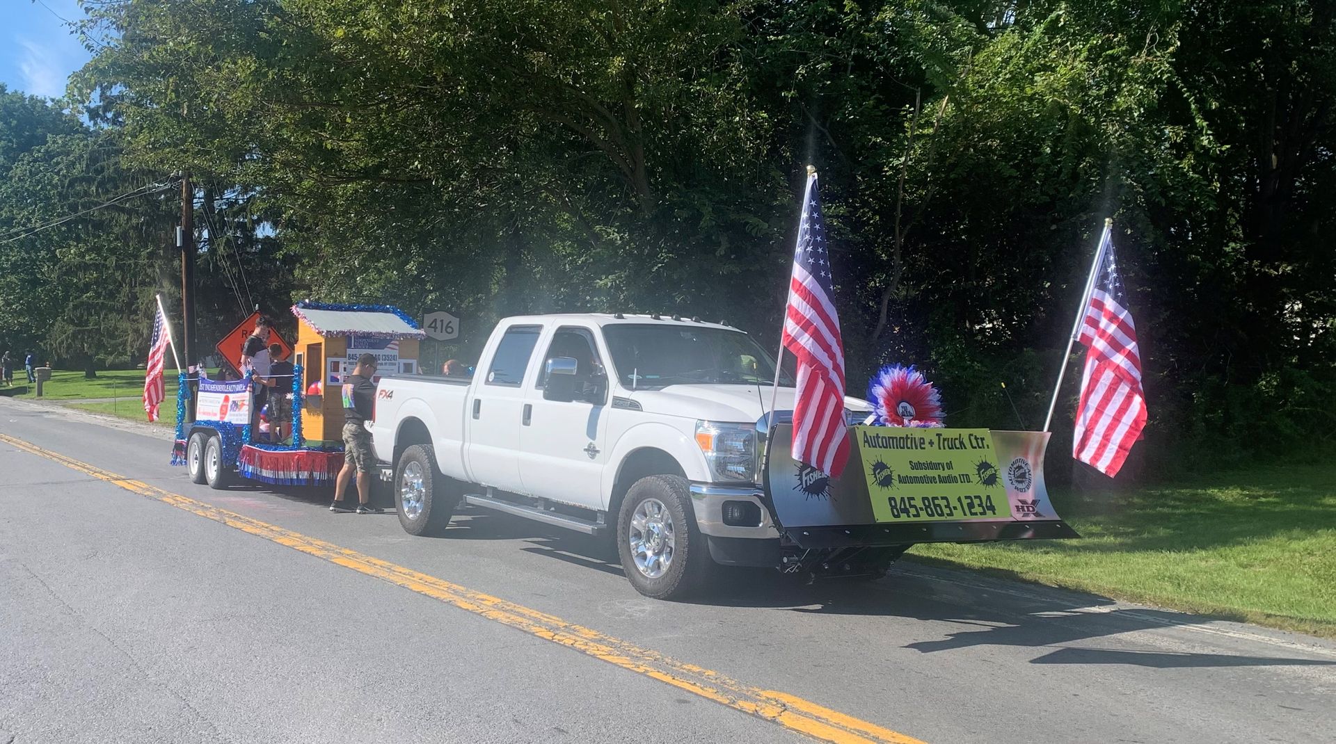 A white truck with an american flag on the back is parked on the side of the road.