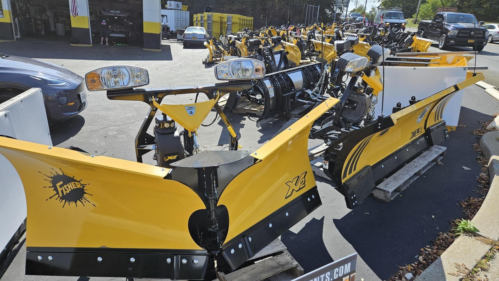 A lot of yellow snow plows are parked in a parking lot