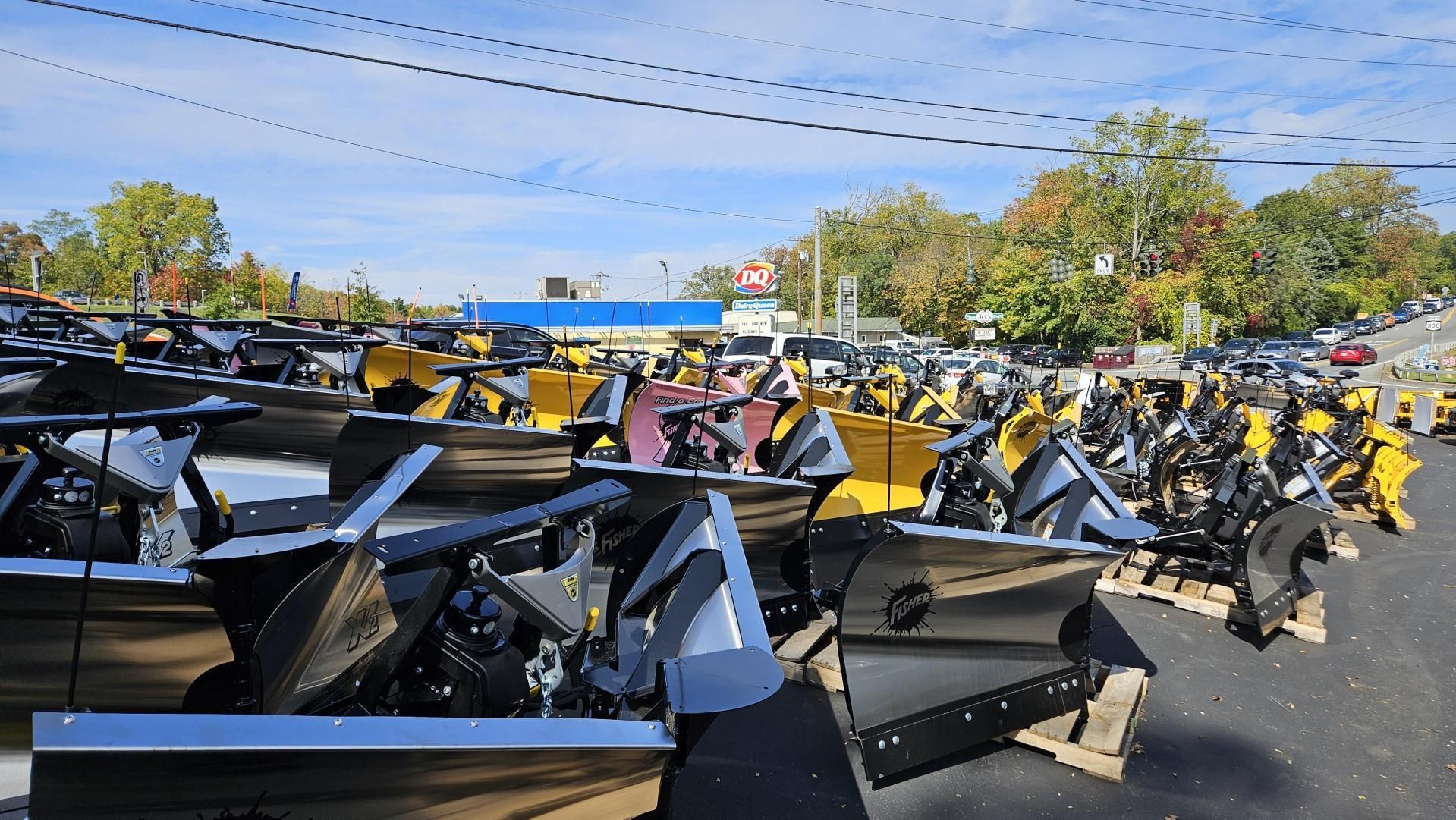 A lot of snow plows are lined up in a parking lot