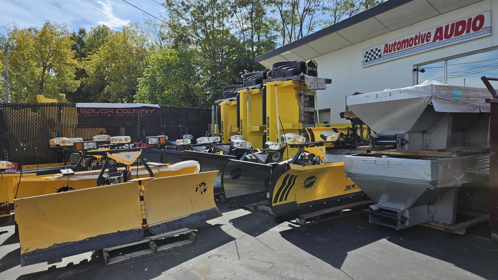 A row of yellow snow plows are parked in front of a building that says american audio.