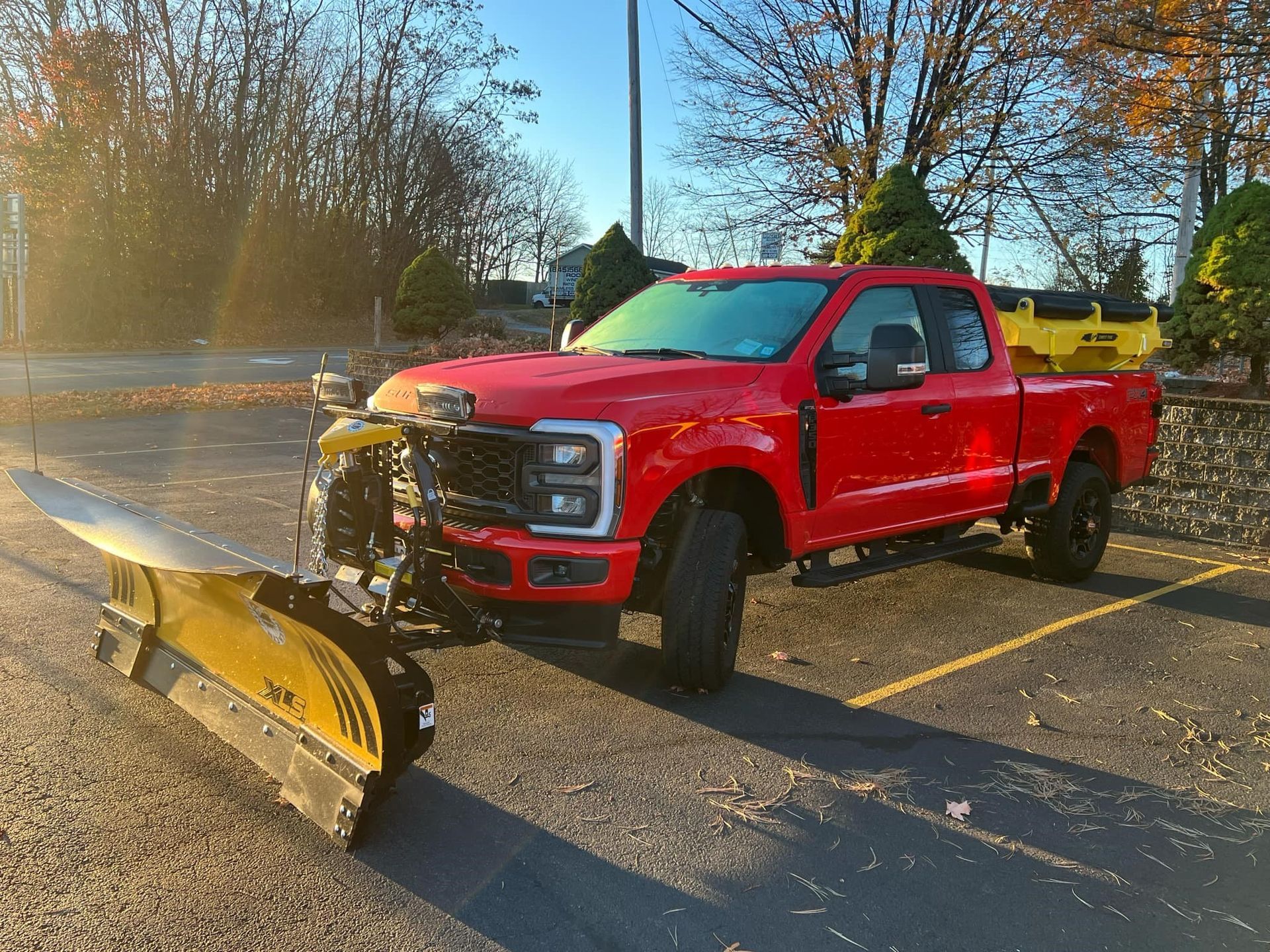 A red truck with a snow plow attached to it is parked in a parking lot.
